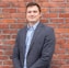 man in gray suit jacket standing beside brown brick wall